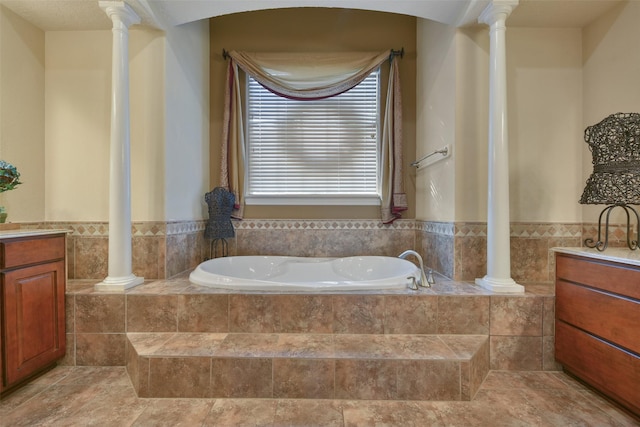 bathroom featuring ornate columns, vanity, and a relaxing tiled tub