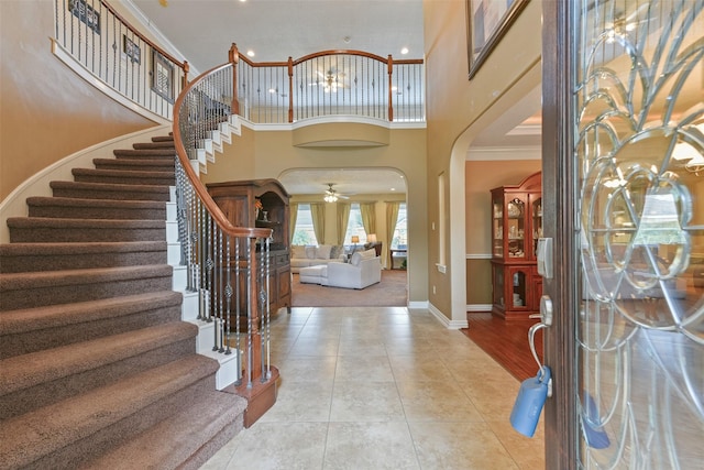 entryway with light tile patterned floors, a towering ceiling, ceiling fan, and crown molding