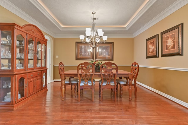 dining space featuring a notable chandelier, a raised ceiling, ornamental molding, and light wood-type flooring