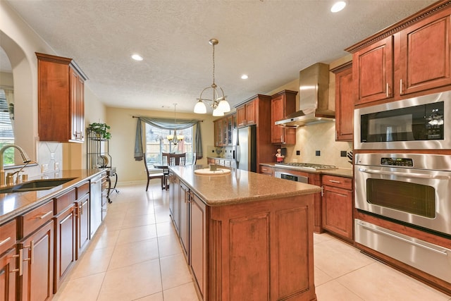 kitchen featuring sink, wall chimney range hood, a chandelier, a kitchen island, and appliances with stainless steel finishes