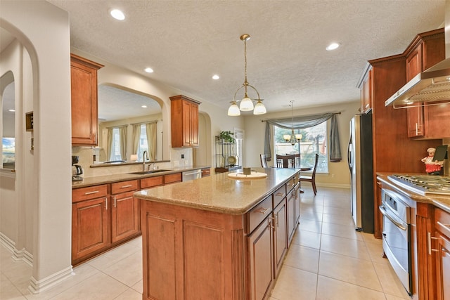 kitchen with sink, a center island, wall chimney exhaust hood, pendant lighting, and appliances with stainless steel finishes