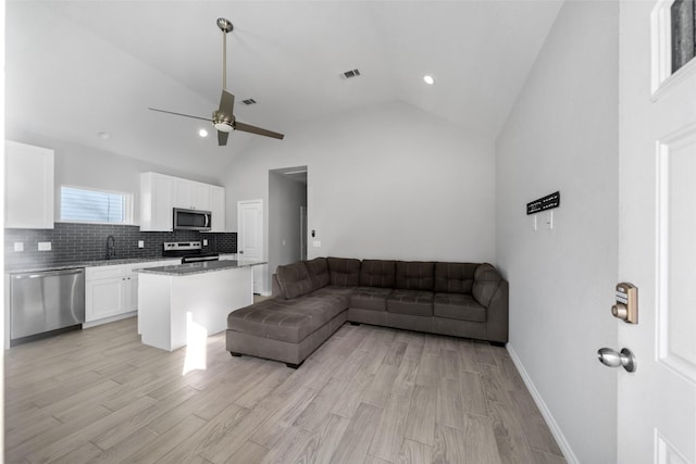 living room with light wood-type flooring, high vaulted ceiling, ceiling fan, and sink