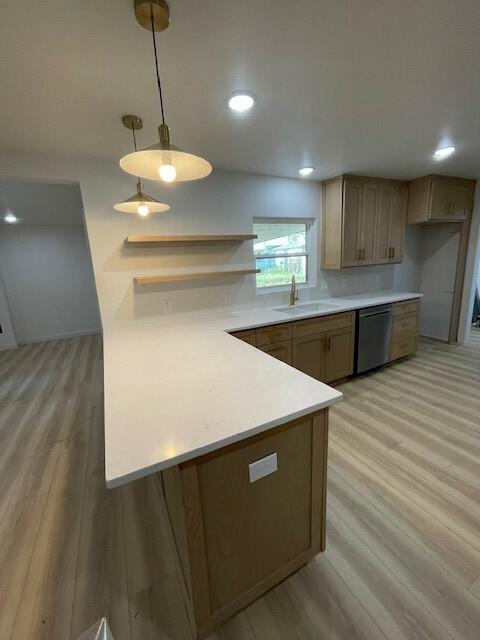 kitchen with kitchen peninsula, stainless steel dishwasher, sink, pendant lighting, and light hardwood / wood-style floors