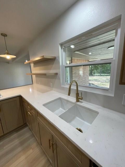 kitchen featuring light stone counters, sink, hanging light fixtures, and light hardwood / wood-style flooring