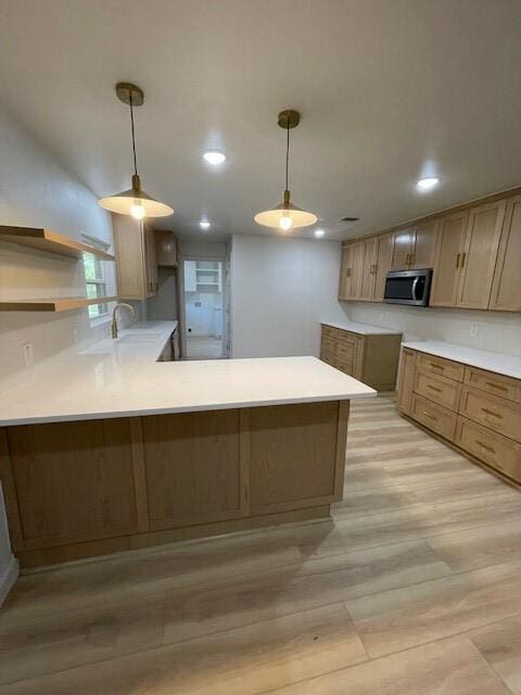 kitchen with kitchen peninsula, sink, pendant lighting, and light hardwood / wood-style floors