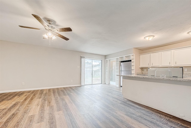 kitchen with white cabinetry, light stone counters, stainless steel fridge, light hardwood / wood-style floors, and fridge