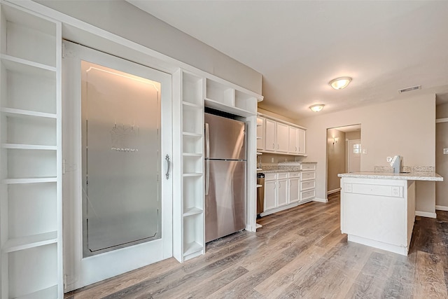 kitchen featuring light stone countertops, hardwood / wood-style flooring, a center island, white cabinetry, and stainless steel refrigerator