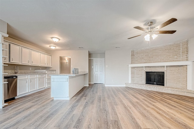 kitchen with dishwasher, white cabinets, ceiling fan, a fireplace, and light hardwood / wood-style floors