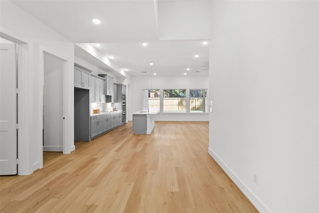 kitchen with a kitchen breakfast bar, gray cabinetry, sink, a center island, and light hardwood / wood-style floors