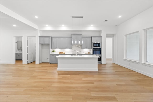 kitchen featuring appliances with stainless steel finishes, gray cabinets, light hardwood / wood-style floors, and an island with sink