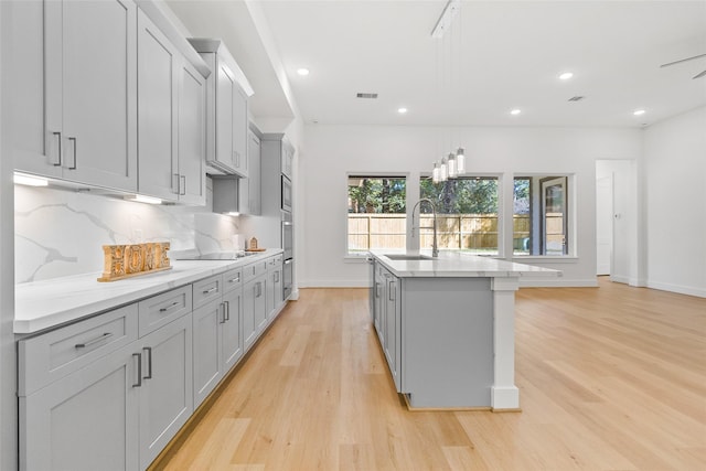 kitchen featuring gray cabinetry, light wood-type flooring, sink, and an island with sink