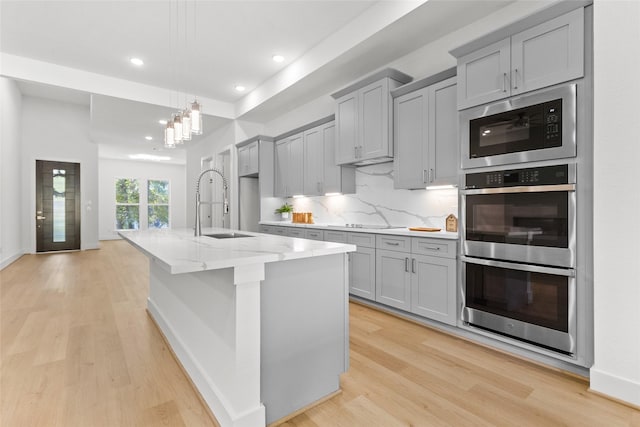 kitchen with gray cabinets, a center island with sink, stainless steel appliances, and light wood-type flooring