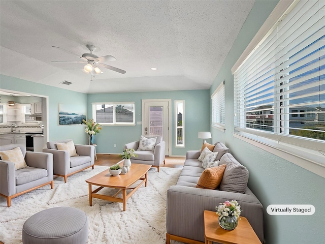 living room with ceiling fan, sink, lofted ceiling, a textured ceiling, and light wood-type flooring