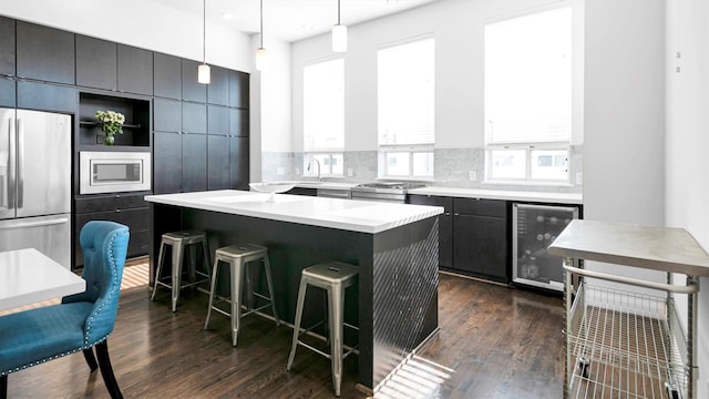 kitchen with hanging light fixtures, wine cooler, dark hardwood / wood-style floors, a kitchen island, and appliances with stainless steel finishes