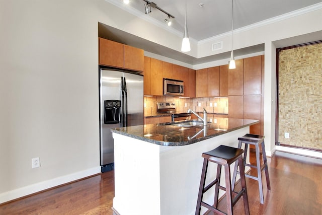 kitchen featuring stainless steel appliances, dark hardwood / wood-style flooring, dark stone countertops, an island with sink, and ornamental molding