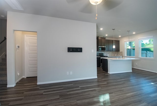 kitchen with dark wood-type flooring, ceiling fan, an island with sink, appliances with stainless steel finishes, and decorative light fixtures