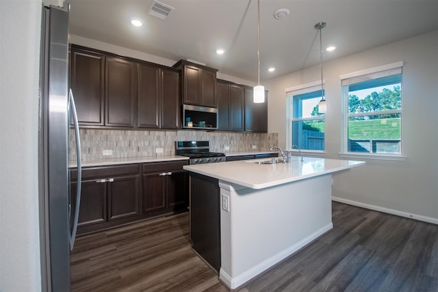 kitchen with appliances with stainless steel finishes, decorative light fixtures, a kitchen island with sink, and dark wood-type flooring