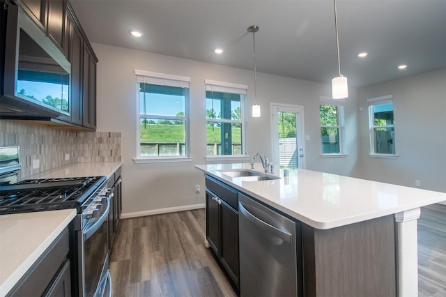 kitchen with pendant lighting, a center island with sink, sink, appliances with stainless steel finishes, and dark hardwood / wood-style flooring