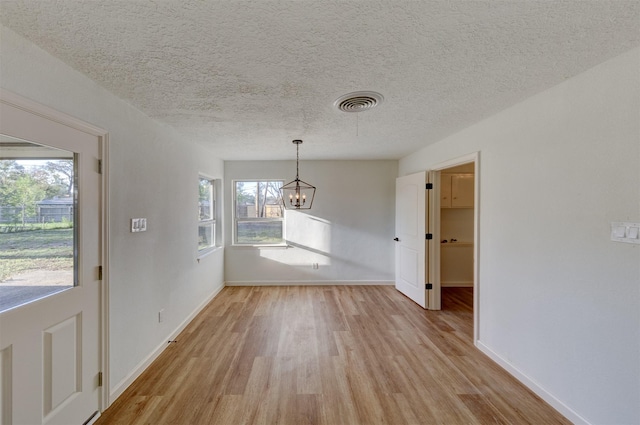 unfurnished dining area with light hardwood / wood-style floors, a textured ceiling, and an inviting chandelier