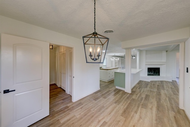 unfurnished dining area with an inviting chandelier, built in shelves, light wood-type flooring, a textured ceiling, and a large fireplace