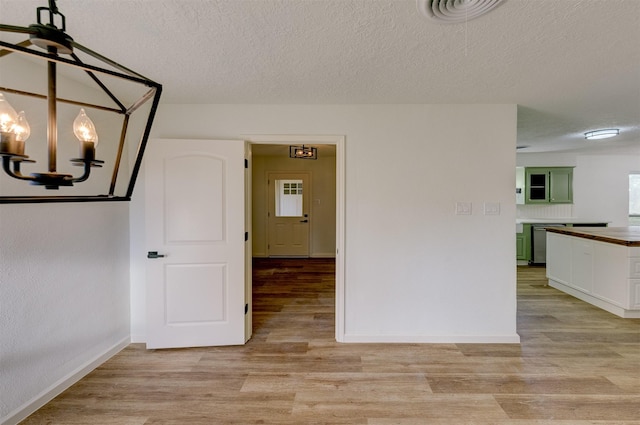 unfurnished dining area featuring a textured ceiling, an inviting chandelier, and light hardwood / wood-style flooring