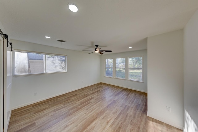 unfurnished room featuring a barn door, ceiling fan, and light hardwood / wood-style floors