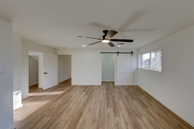 unfurnished bedroom with ceiling fan, a barn door, and light hardwood / wood-style flooring