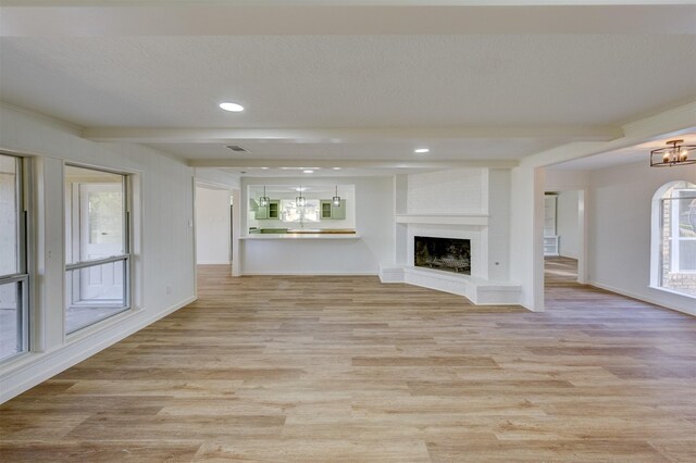 unfurnished living room with a large fireplace, built in shelves, a wealth of natural light, and light hardwood / wood-style flooring