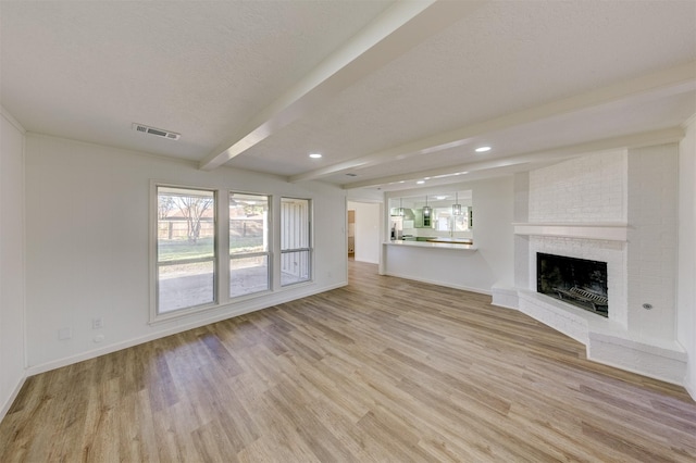 unfurnished living room featuring beam ceiling, light hardwood / wood-style floors, a textured ceiling, and a brick fireplace