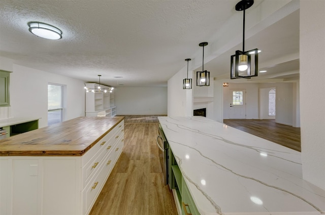 kitchen featuring wooden counters, a textured ceiling, pendant lighting, light hardwood / wood-style floors, and white cabinetry