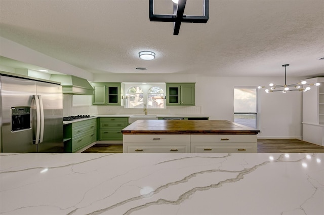 kitchen featuring wood counters, wall chimney range hood, green cabinetry, white cabinets, and stainless steel fridge with ice dispenser