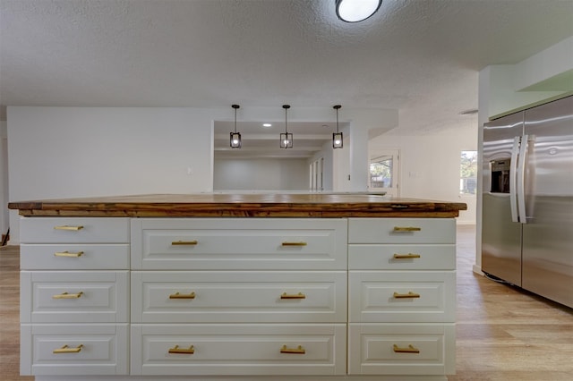 kitchen with white cabinetry, hanging light fixtures, stainless steel fridge, light hardwood / wood-style floors, and a textured ceiling