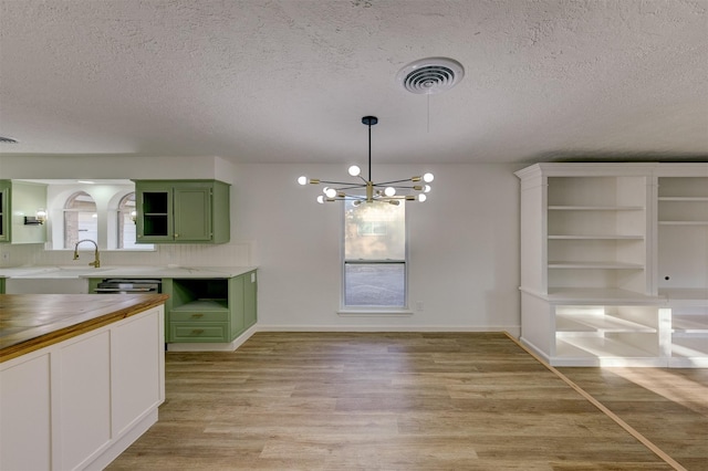 kitchen with green cabinetry, light wood-type flooring, a textured ceiling, a notable chandelier, and butcher block counters