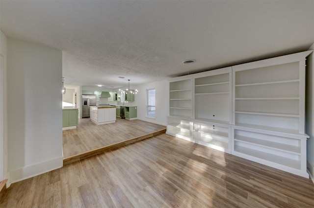 unfurnished living room featuring built in shelves, light wood-type flooring, a textured ceiling, and an inviting chandelier