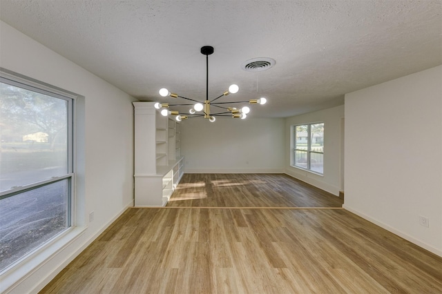 unfurnished dining area featuring a chandelier, a textured ceiling, and light hardwood / wood-style floors