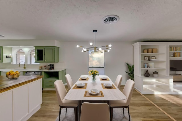 dining room featuring sink, a notable chandelier, a textured ceiling, and light wood-type flooring