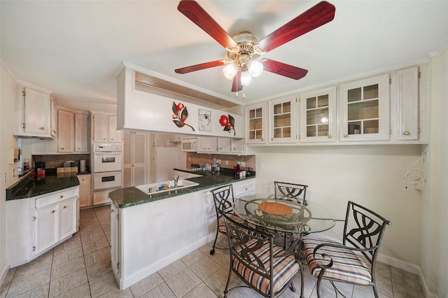 kitchen with white appliances, kitchen peninsula, ceiling fan, tasteful backsplash, and white cabinetry