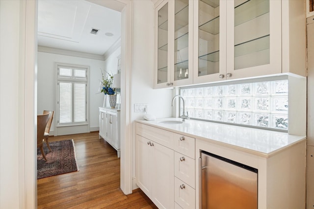 kitchen with stainless steel refrigerator, white cabinetry, sink, crown molding, and light hardwood / wood-style flooring