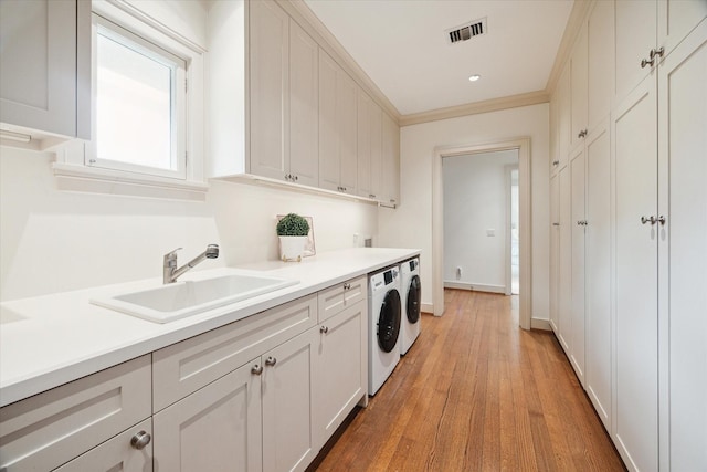 laundry area with sink, cabinets, ornamental molding, washing machine and dryer, and light wood-type flooring