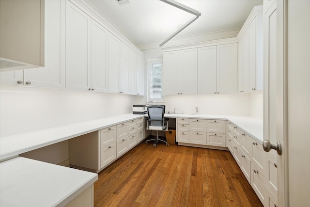 unfurnished office featuring dark wood-type flooring, built in desk, and ornamental molding