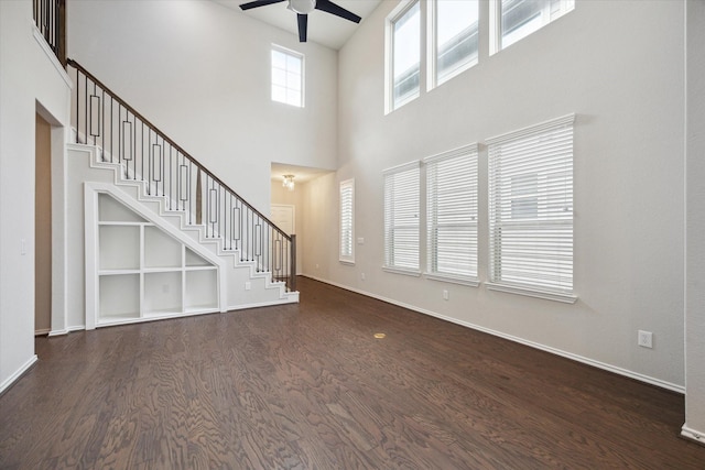 unfurnished living room featuring a towering ceiling, dark hardwood / wood-style flooring, and ceiling fan