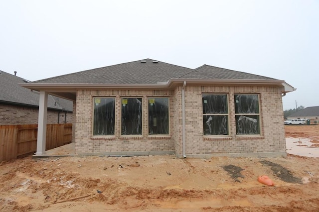 rear view of property with a shingled roof, brick siding, and fence