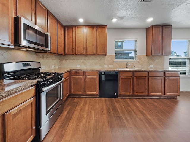 kitchen with a textured ceiling, dark hardwood / wood-style flooring, light stone counters, and appliances with stainless steel finishes