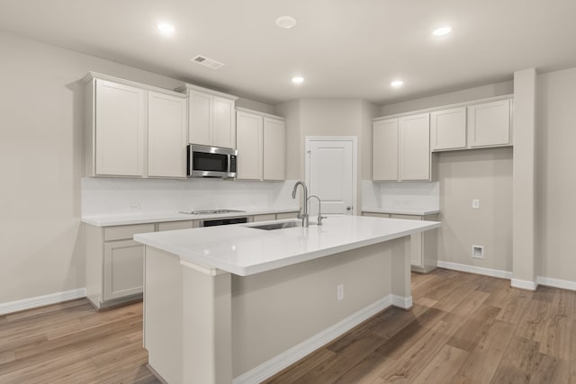 kitchen featuring a center island with sink, white cabinetry, sink, and light hardwood / wood-style flooring