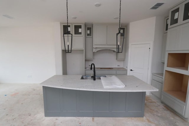 kitchen featuring an island with sink, hanging light fixtures, light stone countertops, sink, and gray cabinets