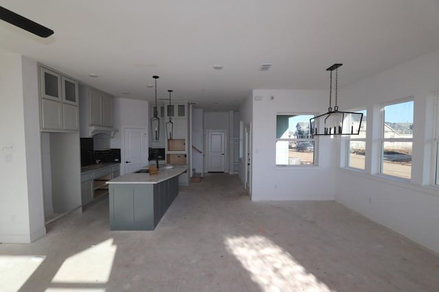 kitchen with glass insert cabinets, decorative light fixtures, a notable chandelier, and an island with sink