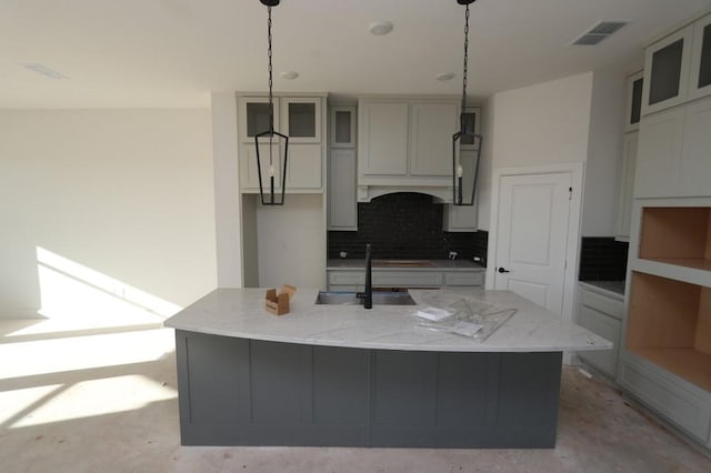 kitchen featuring light stone counters, visible vents, backsplash, a kitchen island with sink, and unfinished concrete floors