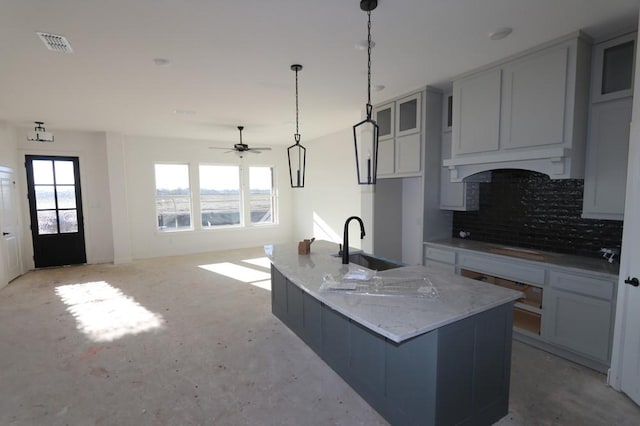 kitchen featuring light stone counters, tasteful backsplash, custom range hood, visible vents, and a sink