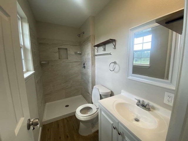 bathroom featuring hardwood / wood-style floors, vanity, toilet, and a tile shower