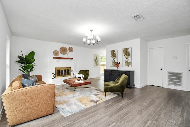 living room featuring a chandelier, a textured ceiling, hardwood / wood-style flooring, and a brick fireplace